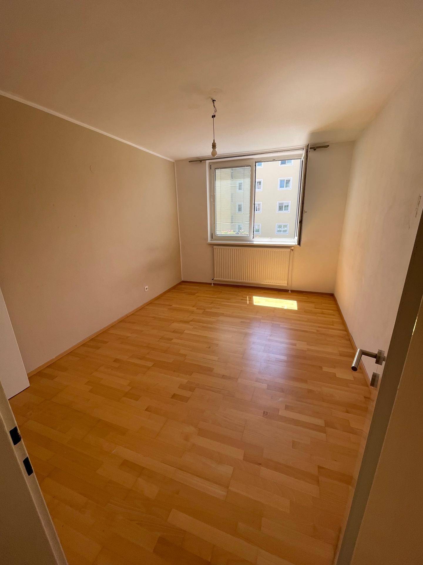 Geräumiges Zimmer mit hellem Parkettboden und großem Fenster, das viel Tageslicht bietet.