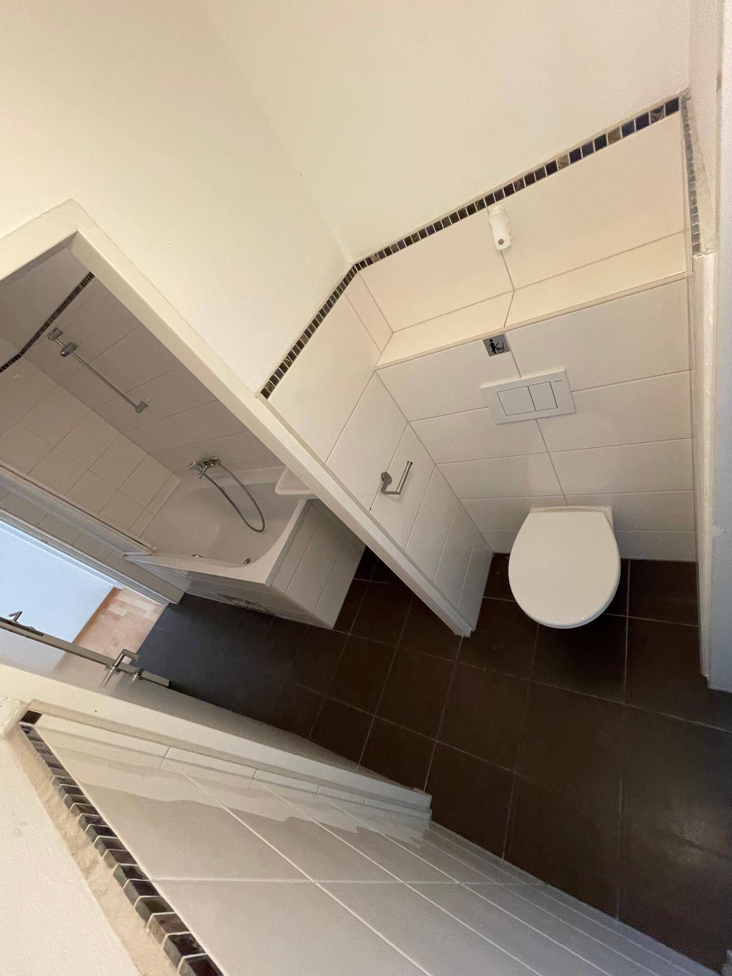 Badezimmer mit Badewanne, Toilette und dunklen Bodenfliesen in einem gepflegten Zustand.