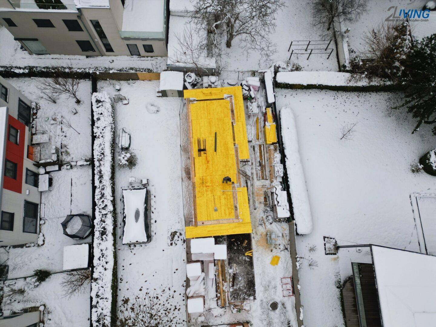Luftaufnahme einer Baustelle im Winter mit schneebedecktem Gelände und gelber Abdeckung.