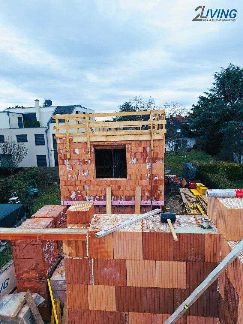 Rohbau eines Hauses mit Ziegelwänden und Holzgerüst, umgeben von Baumaterialien.