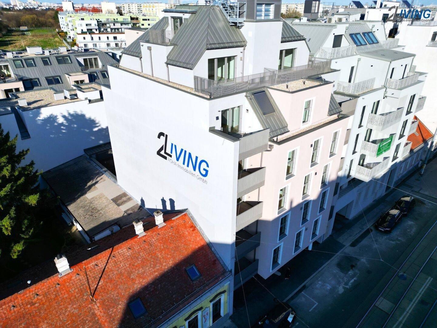 Luftaufnahme eines modernen Wohnkomplexes mit mehreren Balkonen und Dachterrassen in städtischer Umgebung.
