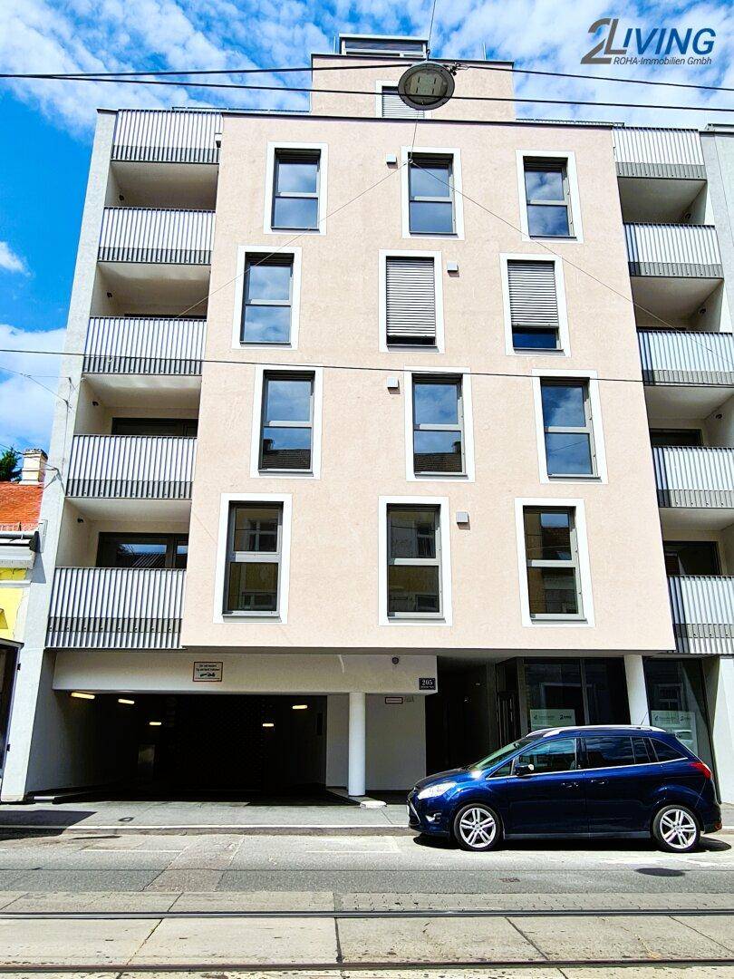 Moderne Gebäudefassade mit Balkonen, großen Fenstern und Tiefgaragenzufahrt an einer städtischen Straße.