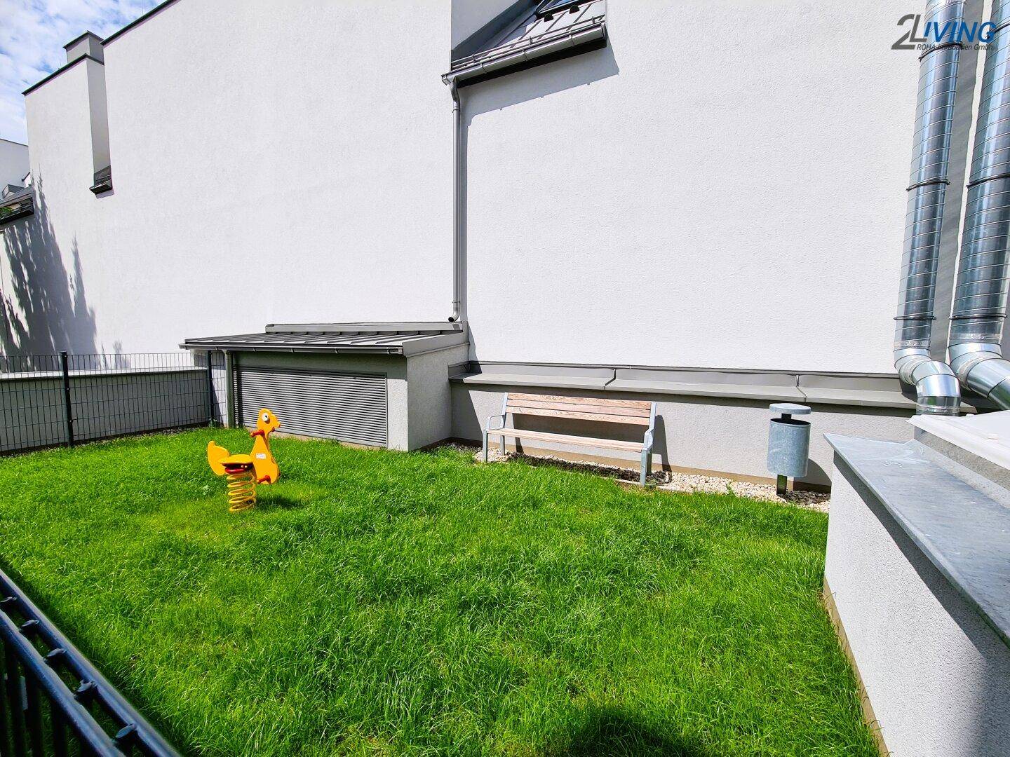 Kleiner Gartenbereich mit Spielgerät und Sitzbank neben dem modernen Wohngebäude.