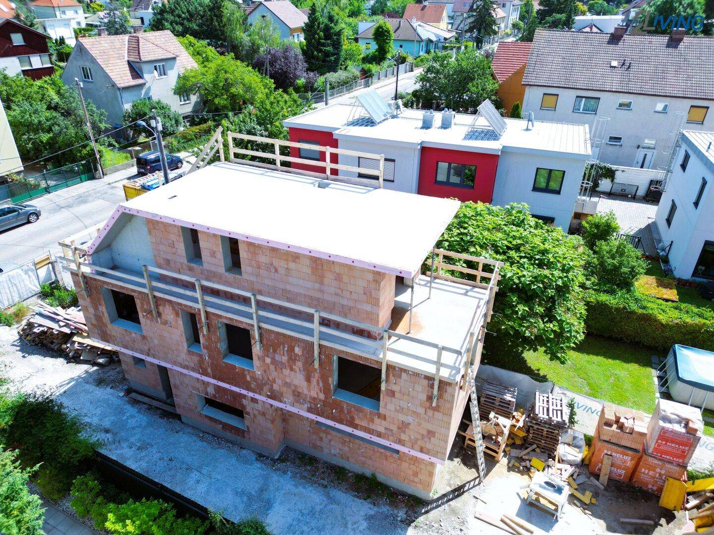 Luftaufnahme eines im Bau befindlichen Hauses mit Rohbau und Flachdach in einer Wohnsiedlung.