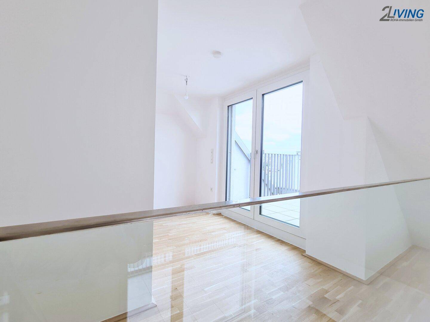 Blick von der Galerie mit Glasbrüstung auf den unteren Wohnbereich und die großen Fenstertüren.