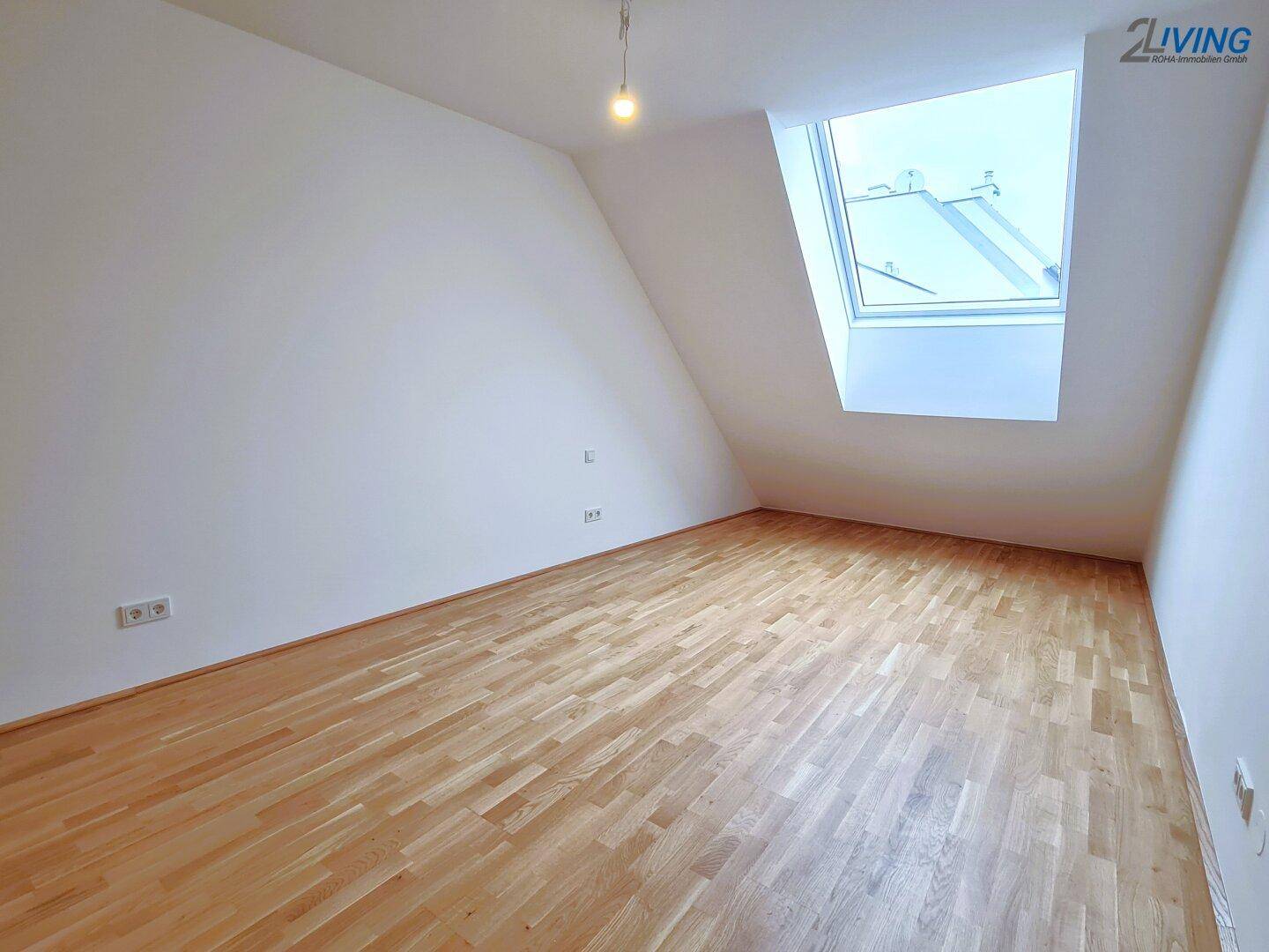 Helles Zimmer im Dachgeschoss mit Holzboden und großem Dachfenster, bietet viel Tageslicht.