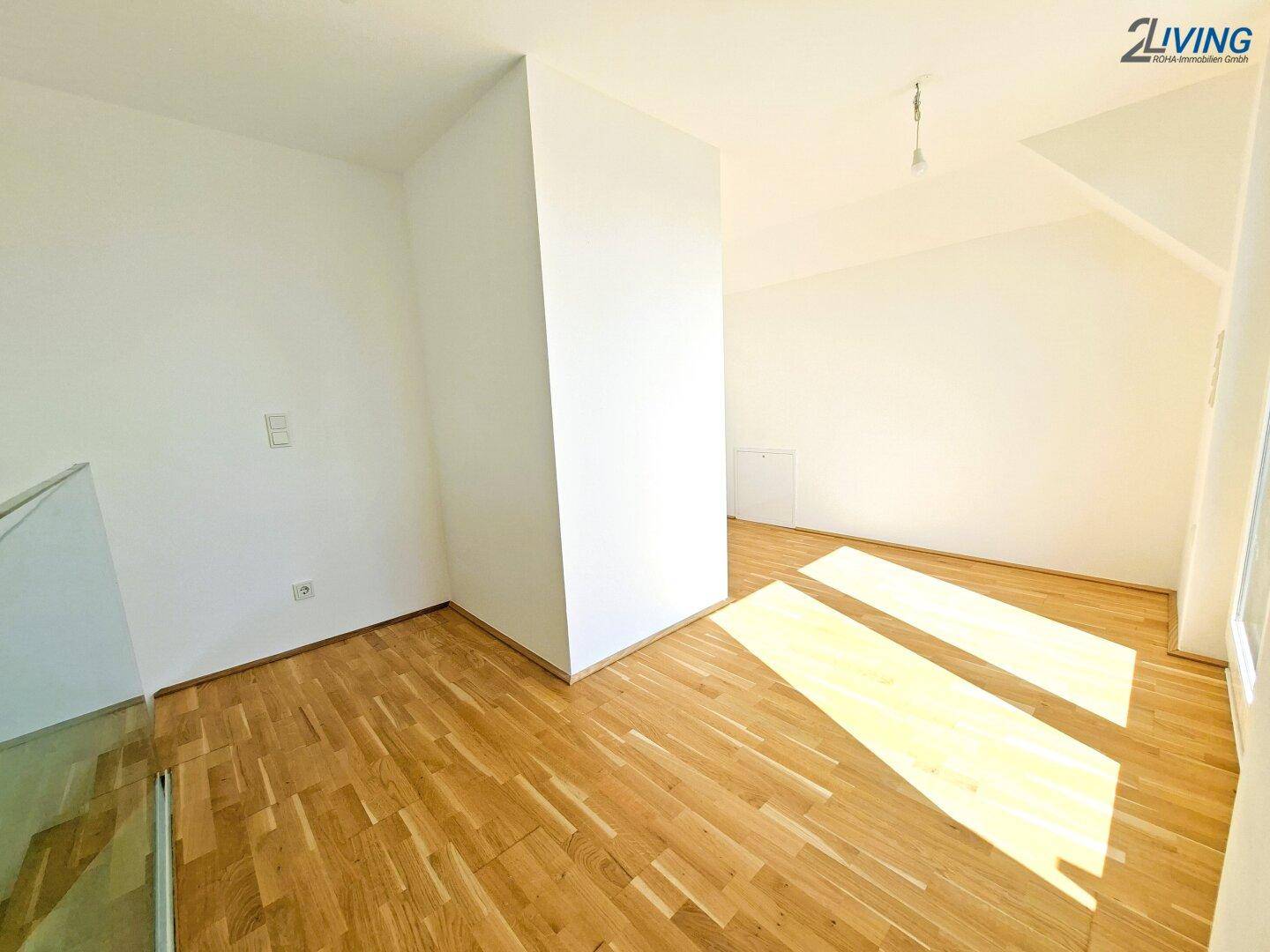 Heller Raum mit Holzparkett und schrägen Wänden, durchflutet von natürlichem Licht.