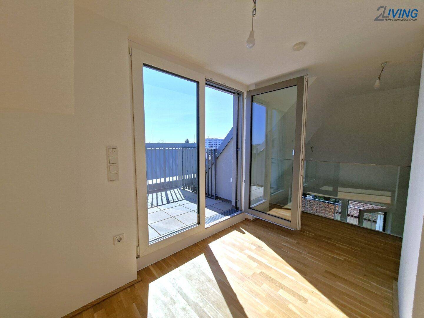 Lichtdurchfluteter Raum mit Holzboden und großen Glastüren zur Dachterrasse.