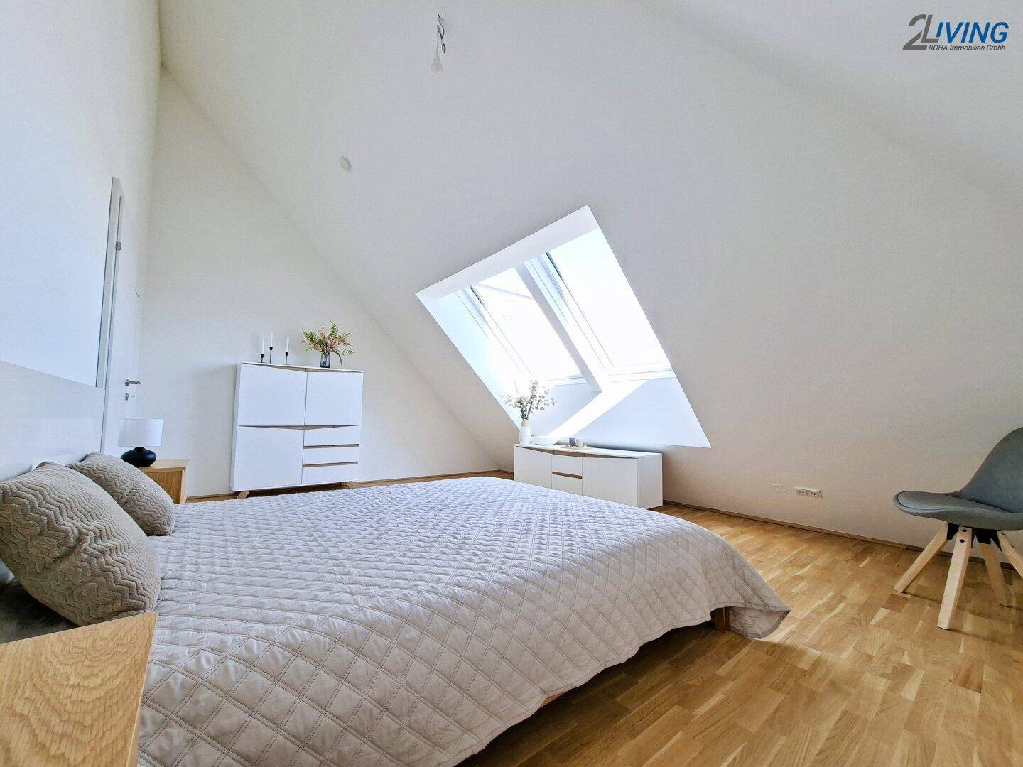 Helles Schlafzimmer im Dachgeschoss mit großen Dachfenstern und Holzboden.