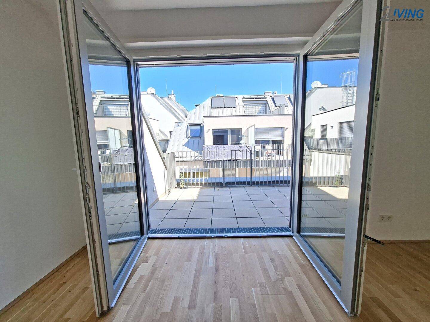 Große Glasfronten öffnen sich zu einer geräumigen Dachterrasse mit Blick auf umliegende Gebäude.