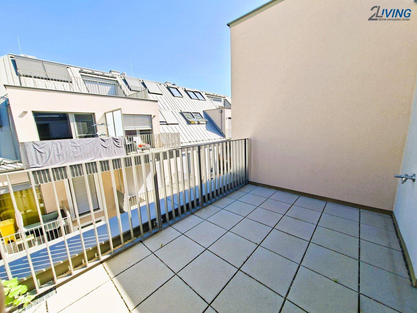 Geräumige, sonnige Dachterrasse mit Fliesenboden und Metallgeländer, umgeben von modernen Gebäuden.