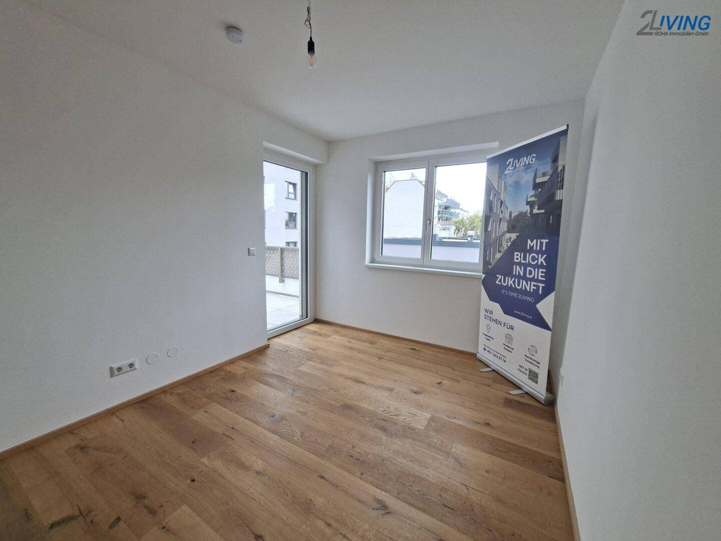 Leeres Zimmer mit Parkettboden, Fenster und Zugang zu einem Außenbereich.