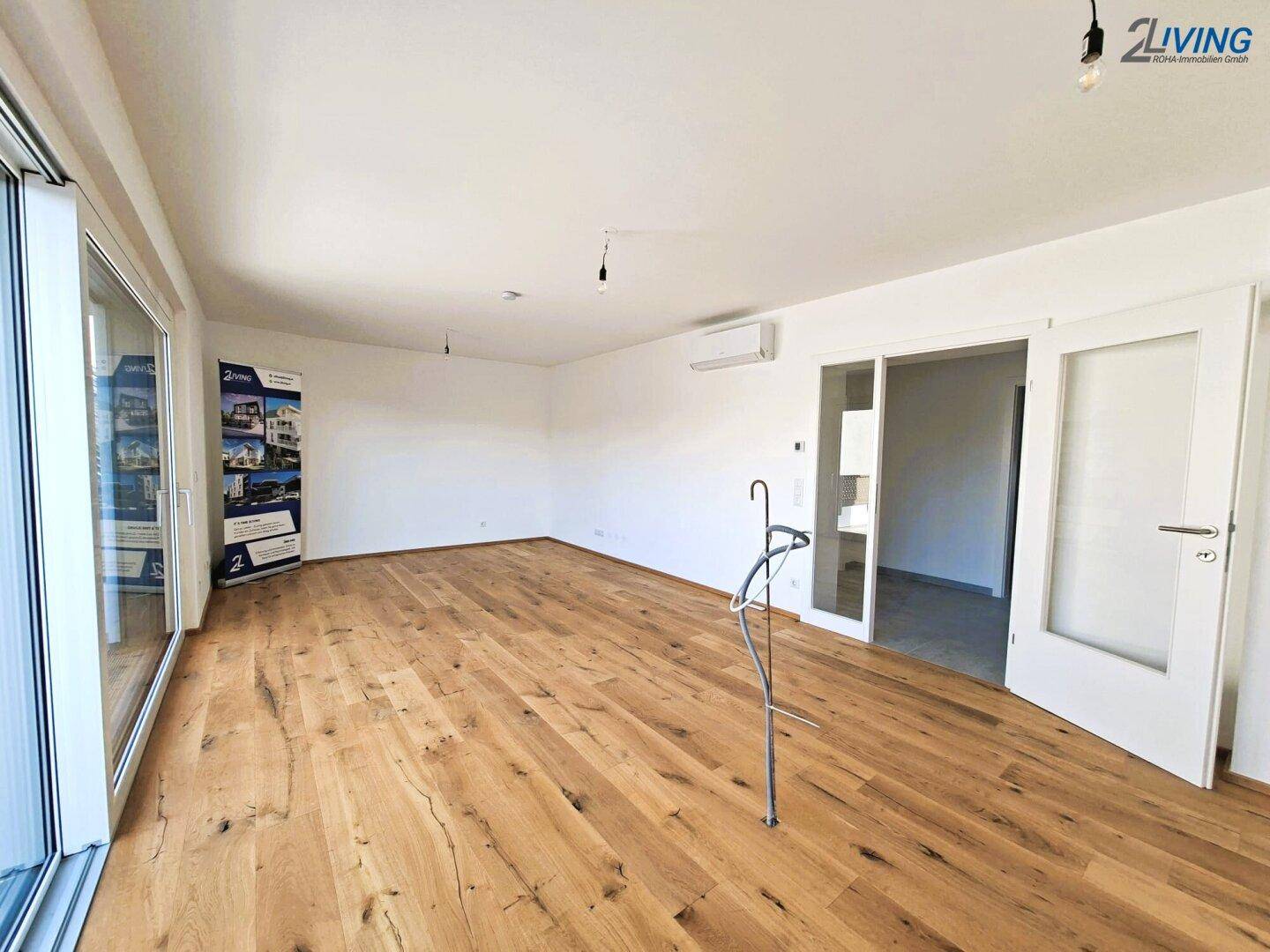 Leeres Wohnzimmer mit Eichenparkett, großen Fenstern und Klimaanlage.