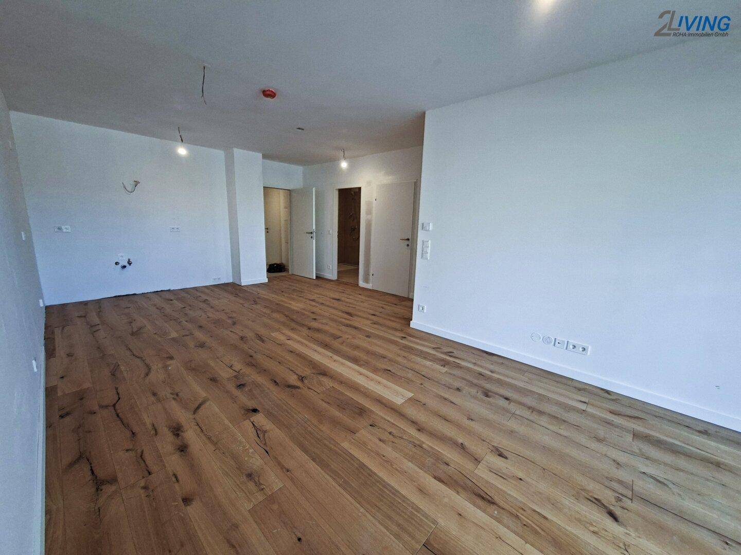 Geräumiger, lichtdurchfluteter Raum mit elegantem Holzboden und weißen Wänden, ideal für offenes Wohnen.