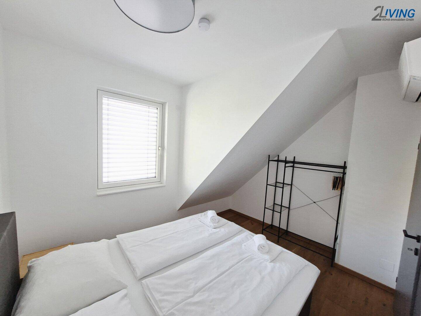 Schlafzimmer mit Doppelbett, Holzboden und Fenster mit Jalousien, unter Dachschräge.