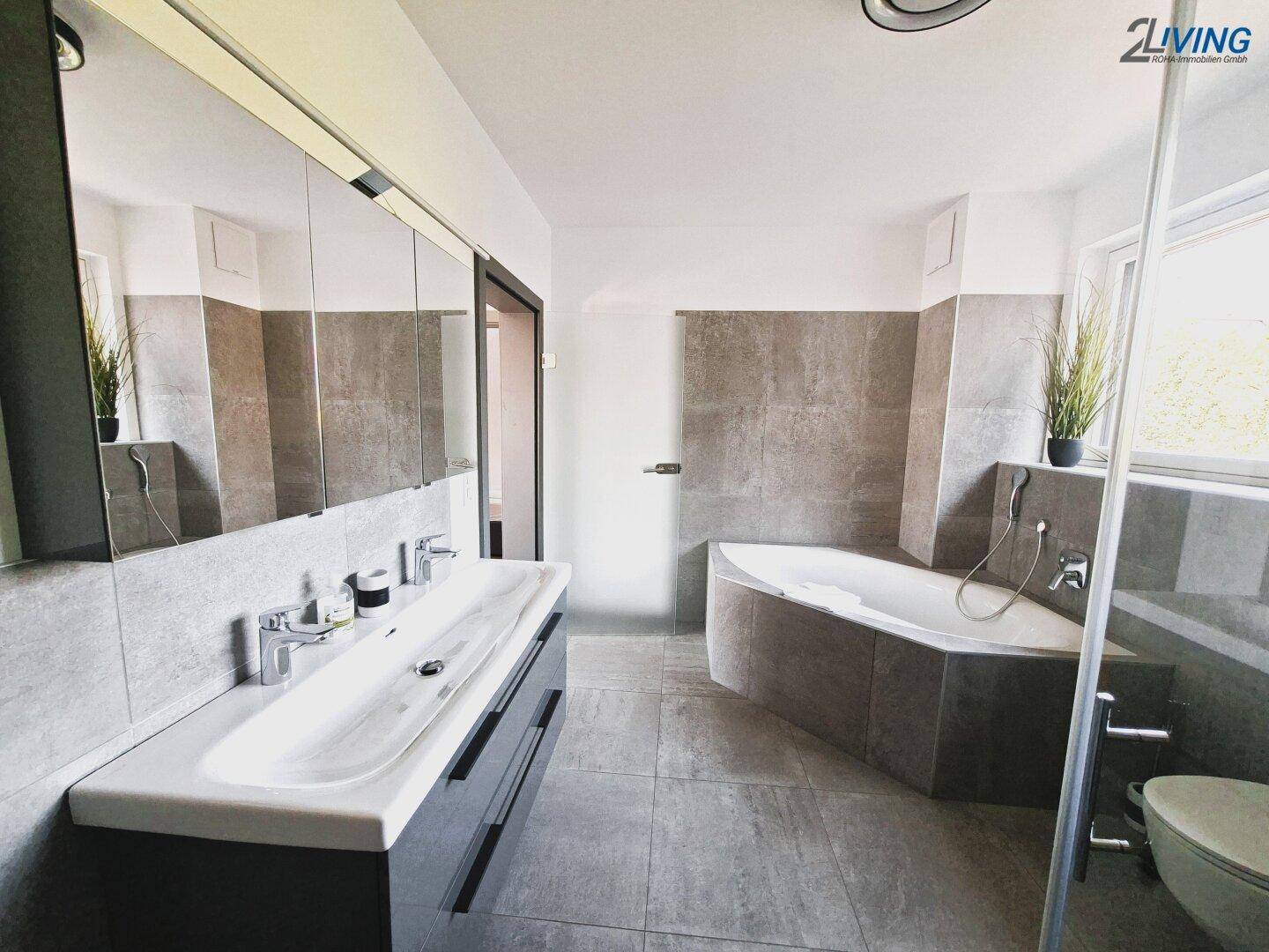 Modernes Badezimmer mit Doppelwaschbecken, Badewanne und grauen Fliesen.