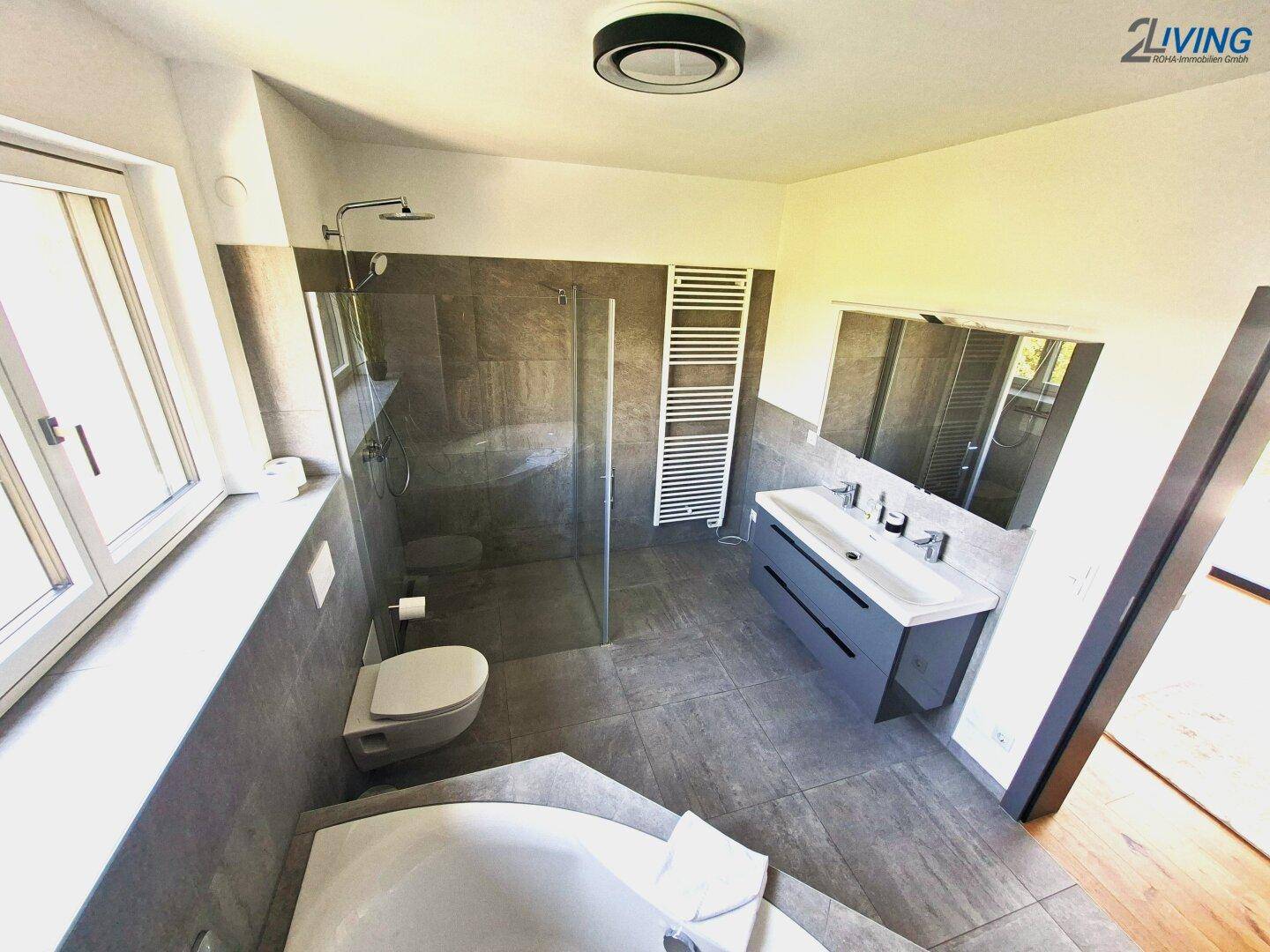 Helles Badezimmer mit Dusche, WC, Doppelwaschbecken und beheiztem Handtuchhalter.