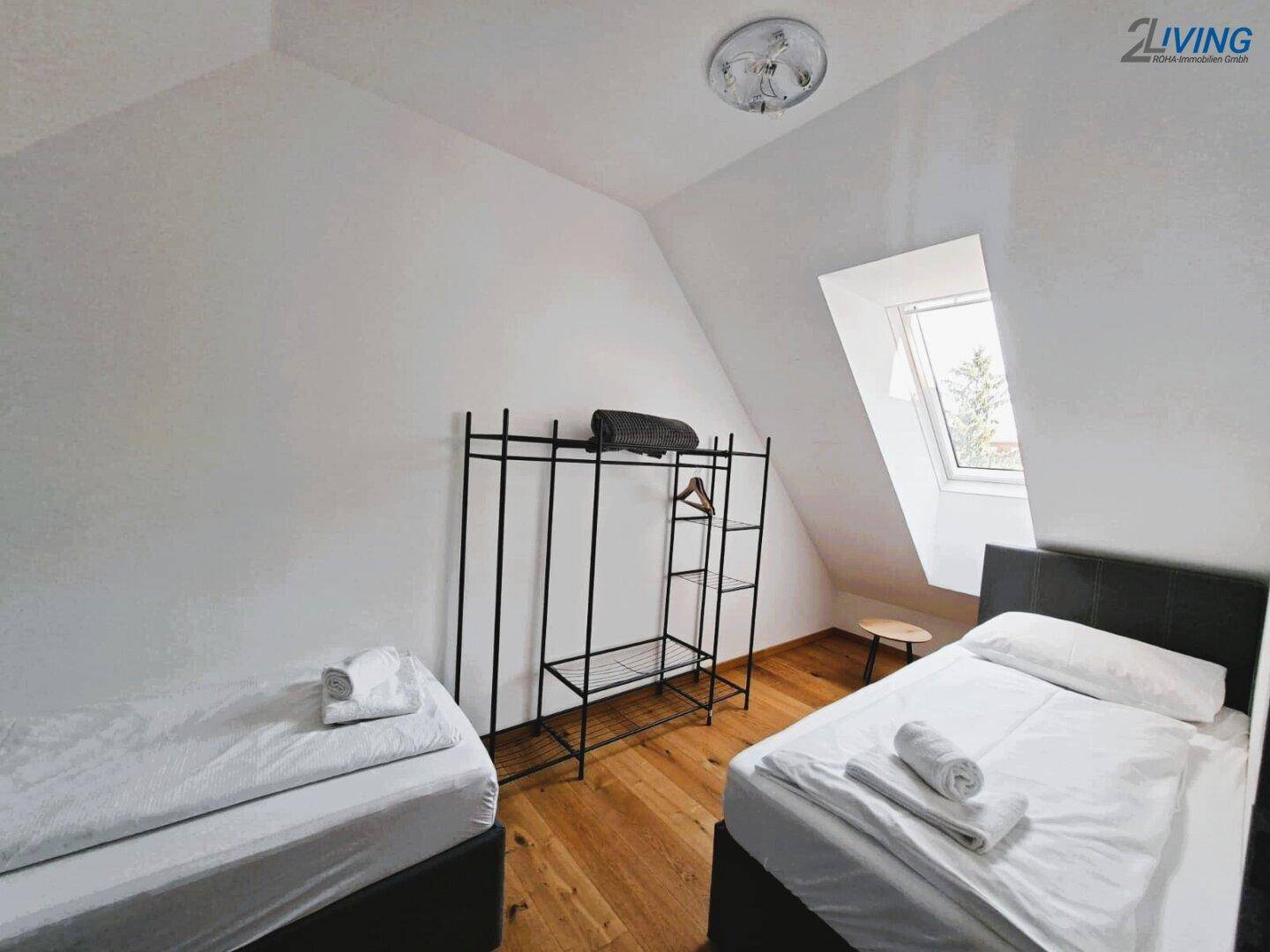Helles Schlafzimmer mit zwei Einzelbetten, Holzboden und Dachfenster.