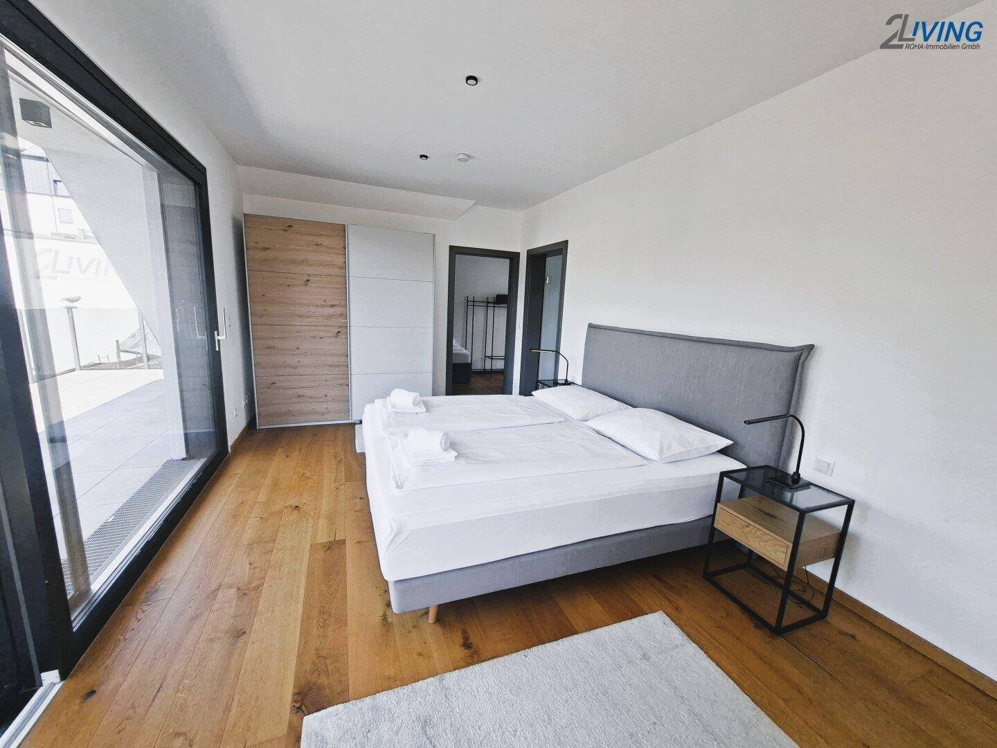 Helles Schlafzimmer mit Holzboden, Doppelbett und Zugang zu einer großen Terrasse.