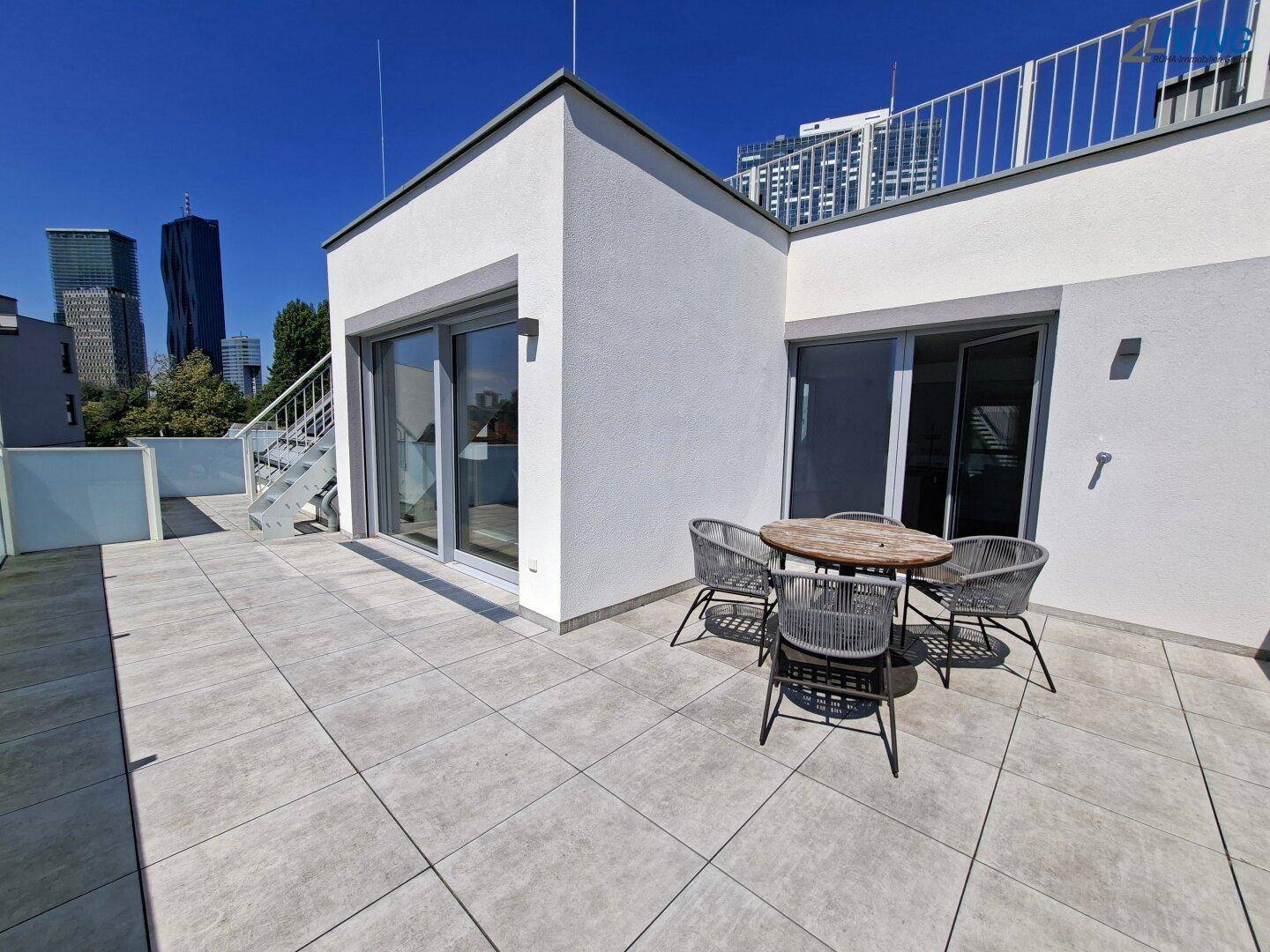 Sonnige Dachterrasse mit Fliesenboden, Sitzgelegenheiten und Blick auf die Stadtkulisse.