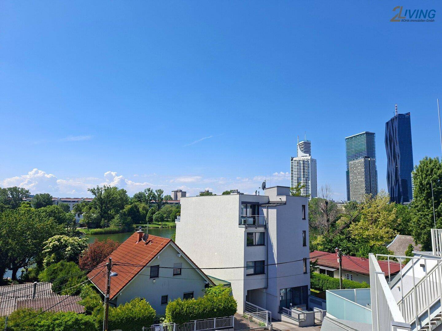 Blick auf ein Wohngebäude mit Fluss im Vordergrund und der Skyline der Stadt im Hintergrund.