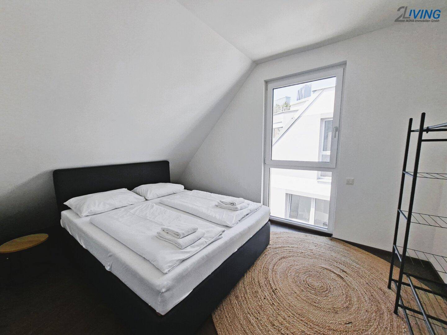 Helles Schlafzimmer mit Dachschräge, großem Fenster und dunklem Holzboden.