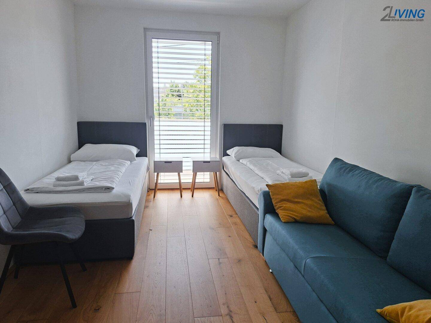 Gemütliches Schlafzimmer mit zwei Einzelbetten, Sofa und Holzboden, ideal als Gästezimmer.