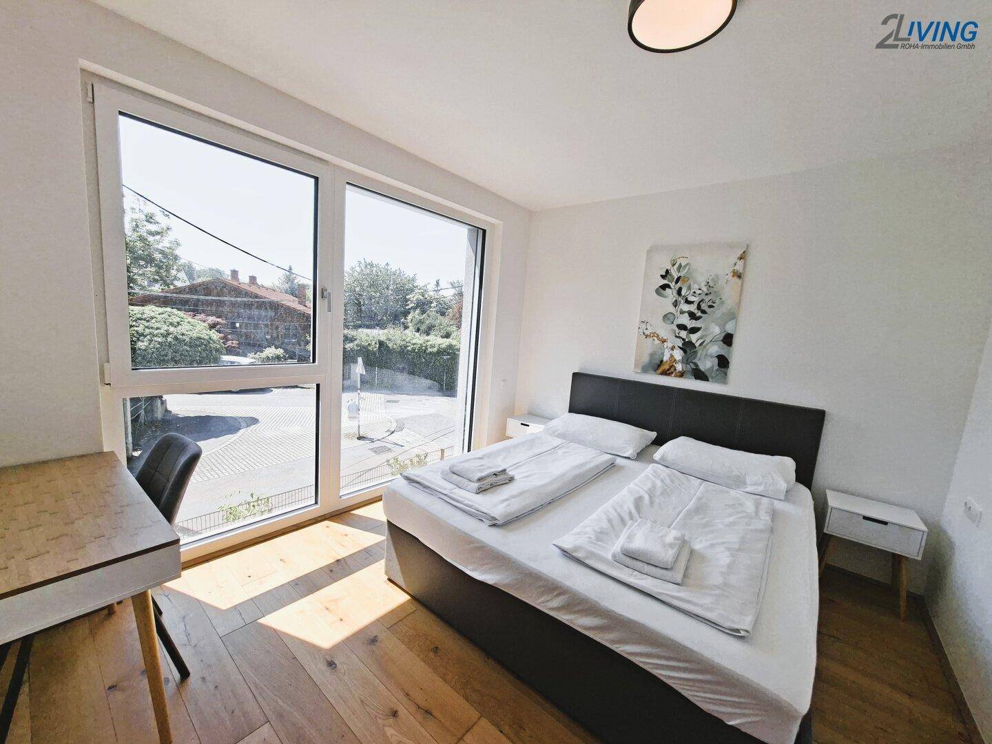 Schlafzimmer mit Doppelbett, Holzboden und großen Fenstern, die einen weiten Blick nach draußen bieten.
