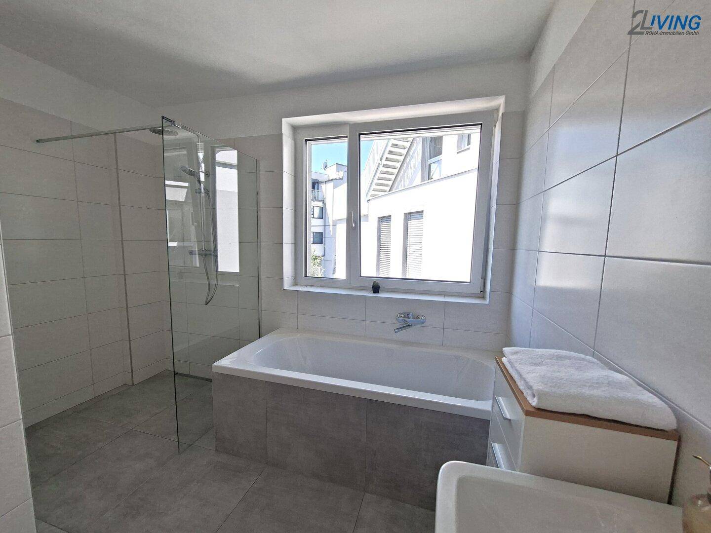 Modernes Badezimmer mit Badewanne, ebenerdiger Dusche und Fenster, komplett gefliest.