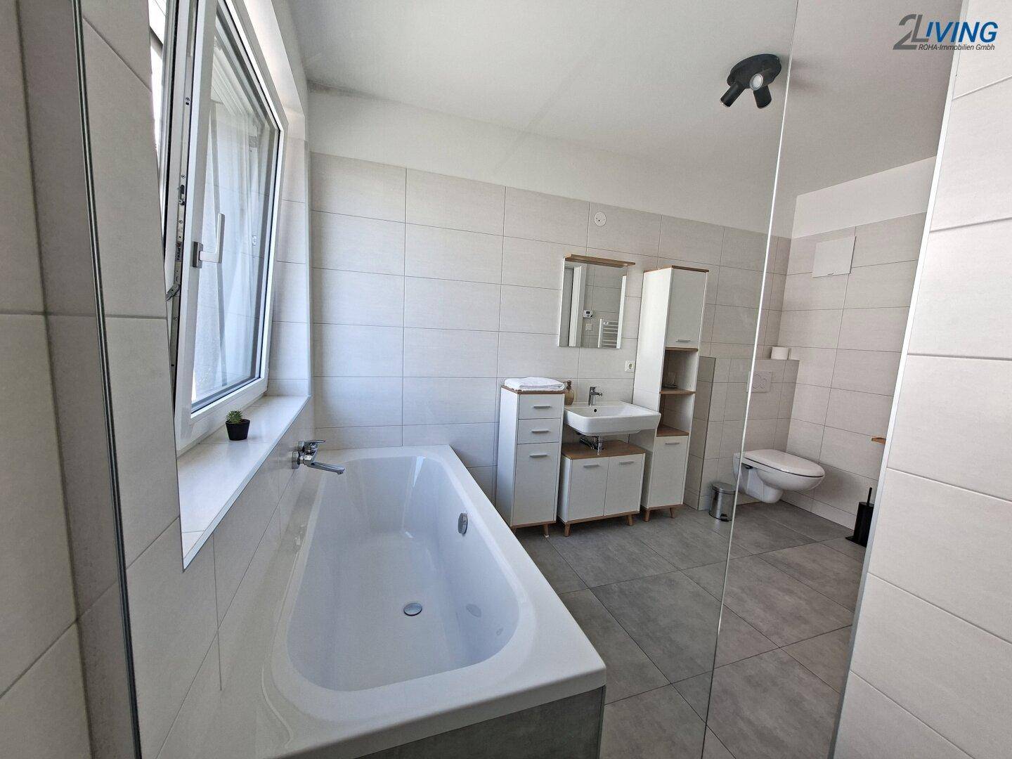 Helles Badezimmer mit Badewanne, Dusche, WC und modernem Waschtisch, ausgestattet mit einem Fenster.