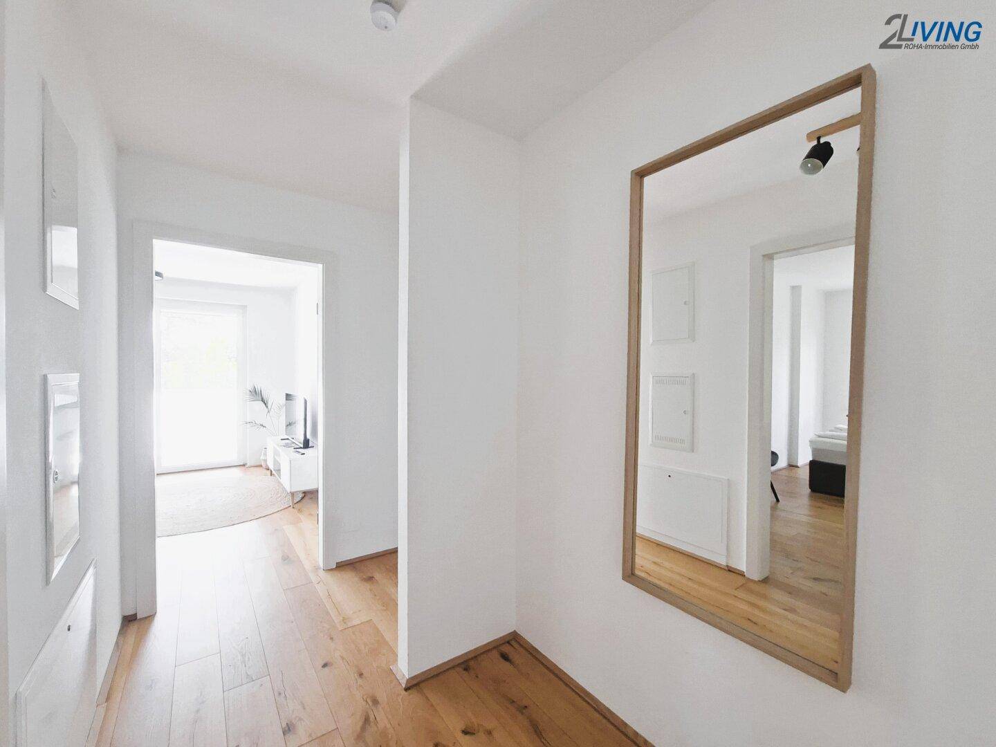 Heller Flur mit Holzfußboden und einem großen Wandspiegel, der den Blick in angrenzende Räume öffnet.