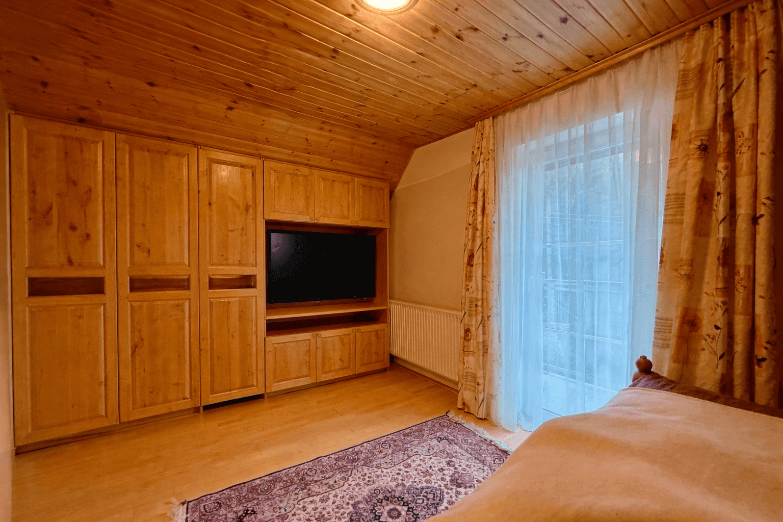 Schlafzimmer mit Holzwänden, Einbauschränken und Zugang zum Balkon, bietet viel Stauraum.