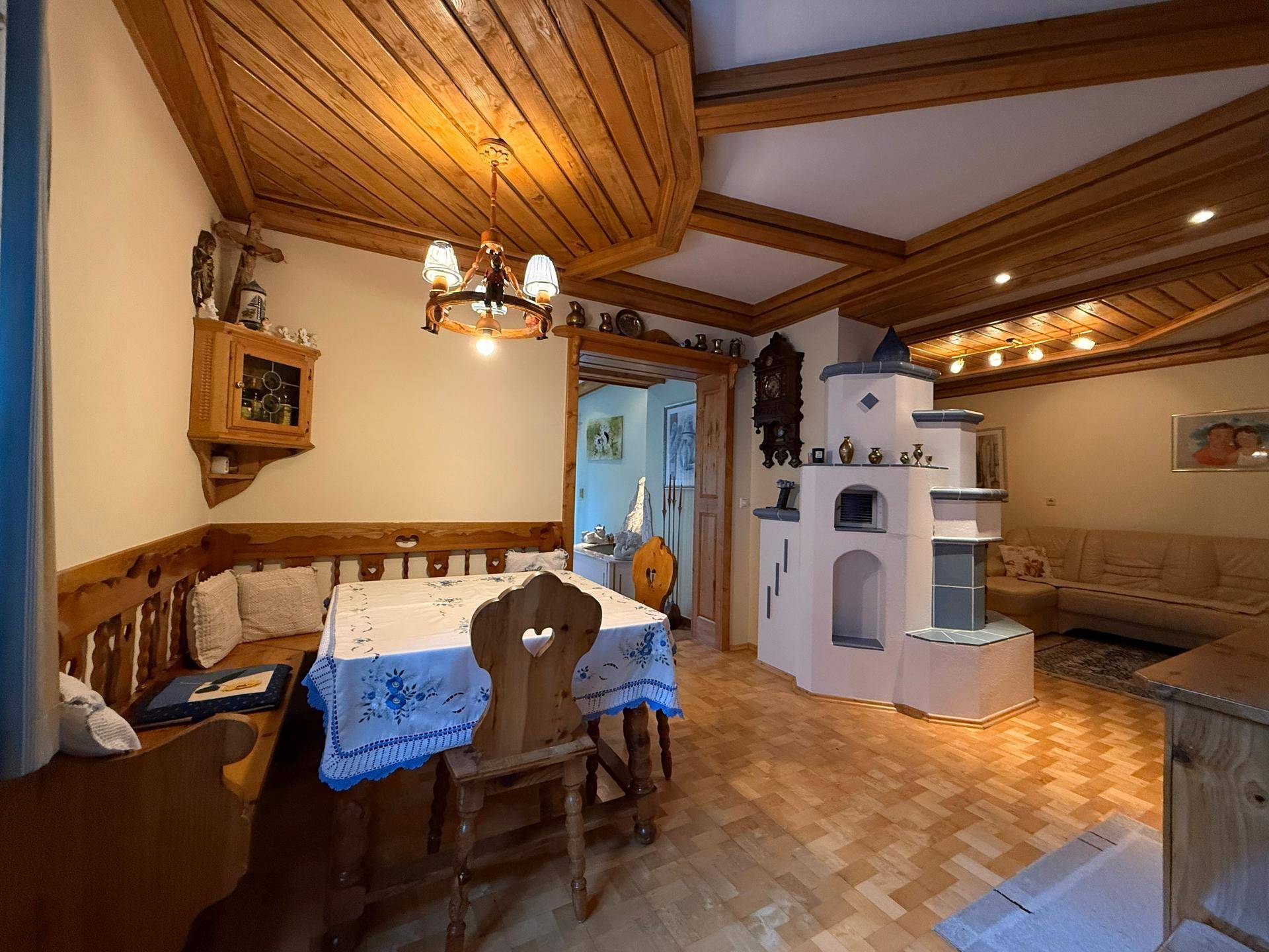 Offener Wohn- und Essbereich mit Kachelofen, Holzbalkendecke und traditionellen Holzmöbeln.