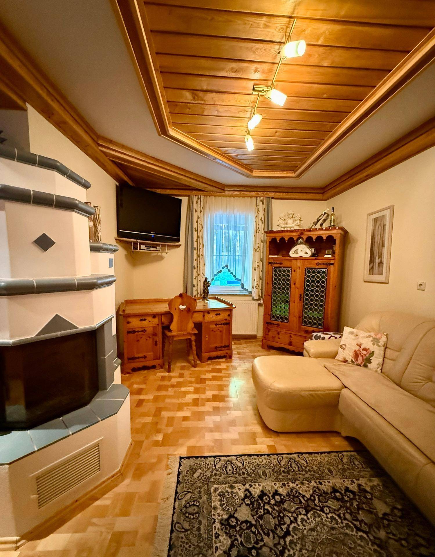 Gemütliches Wohnzimmer im alpinen Stil mit Kachelofen, Holzbalkendecke und traditionellen Möbeln.