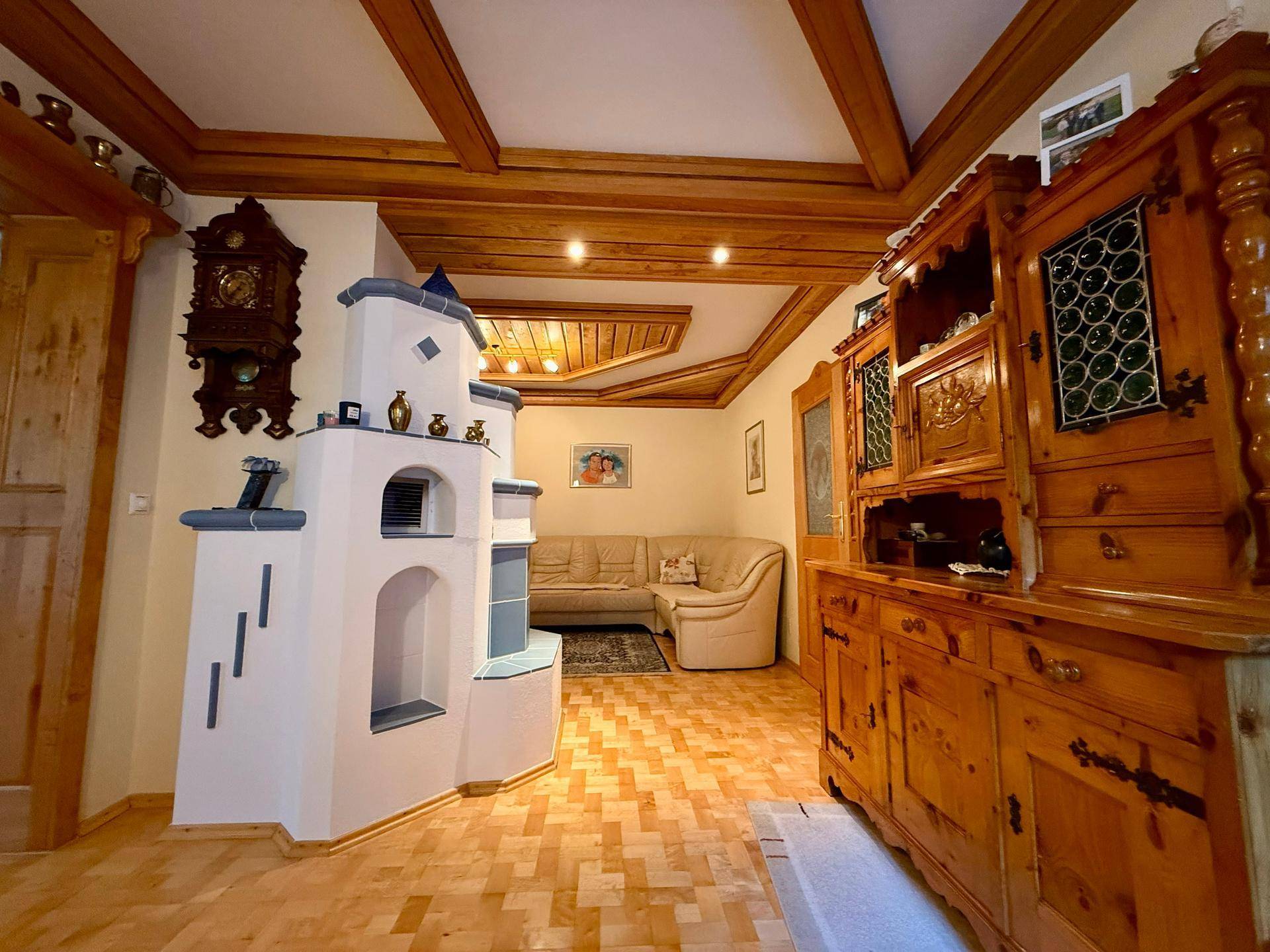 Traditionelles Wohnzimmer mit Kachelofen, Holzbalkendecke und rustikalen Holzmöbeln.