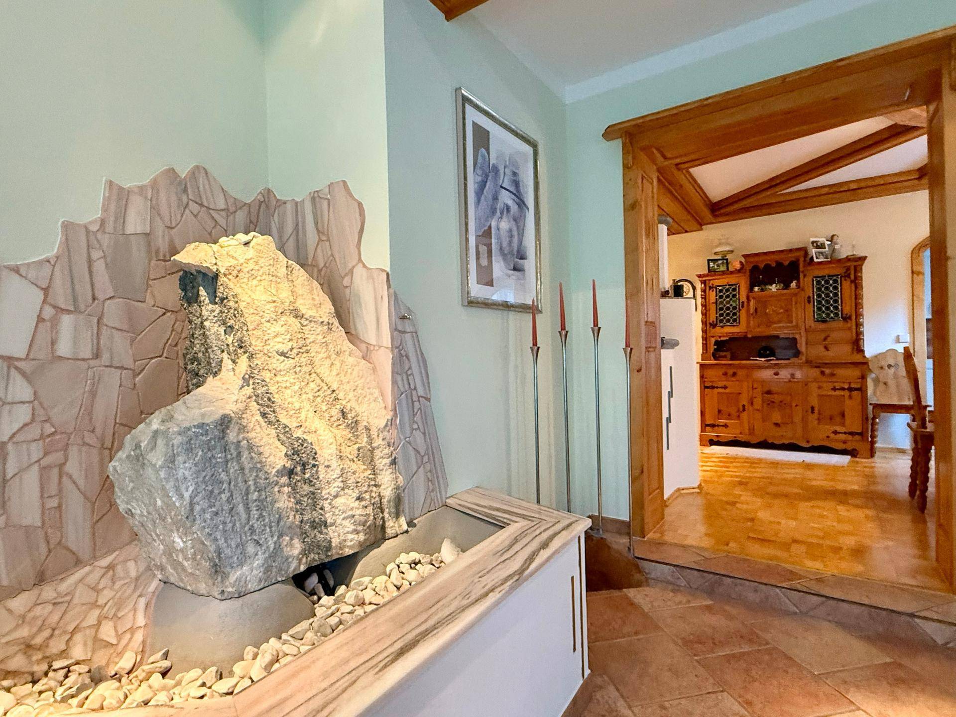 Eingangsbereich mit dekorativem Steinbrunnen und Holztürrahmen, der zu den Wohnräumen führt.