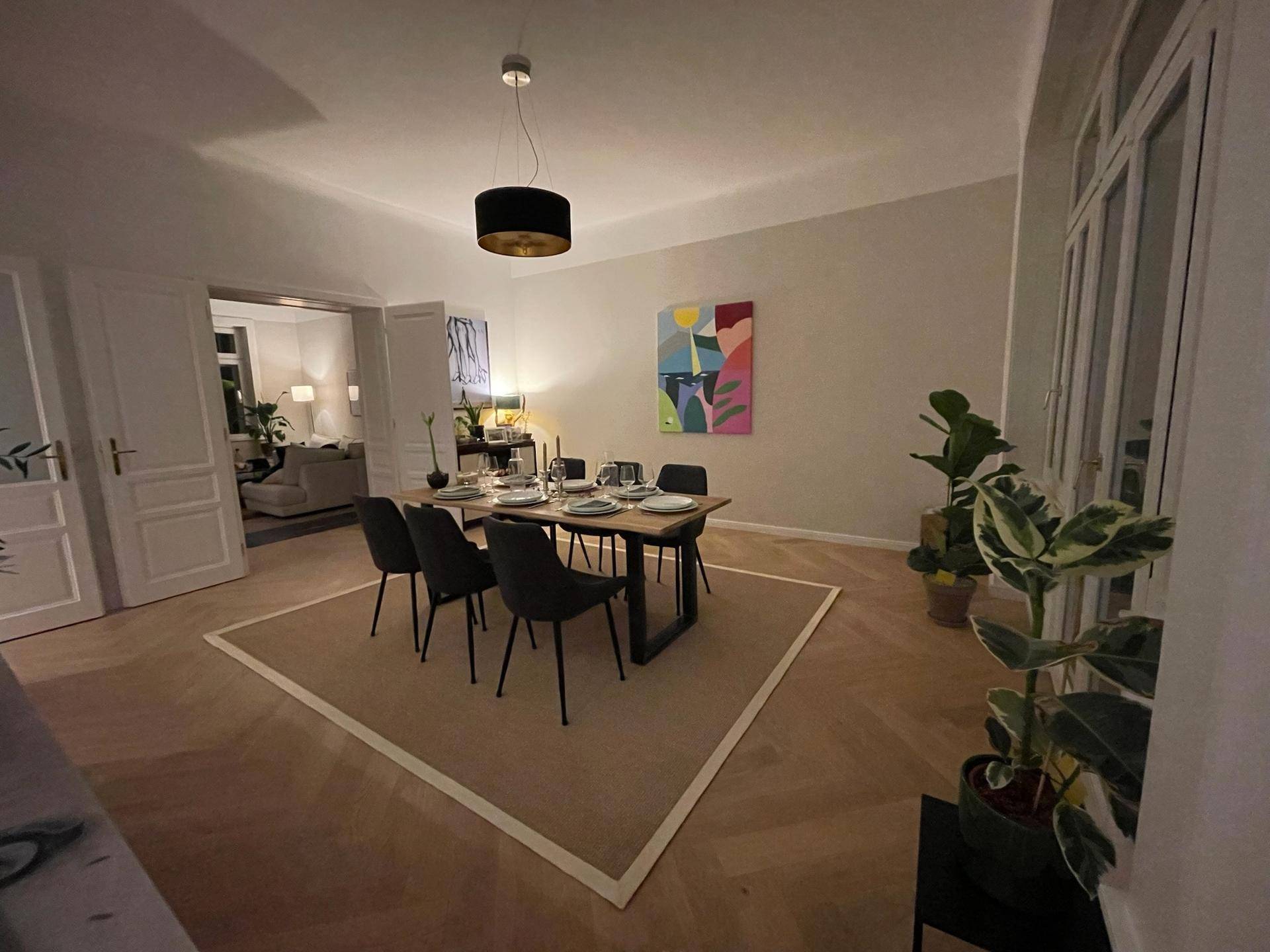 Eleganter Essbereich mit Holztisch, Fischgrätparkett und Blick in den angrenzenden Wohnbereich.