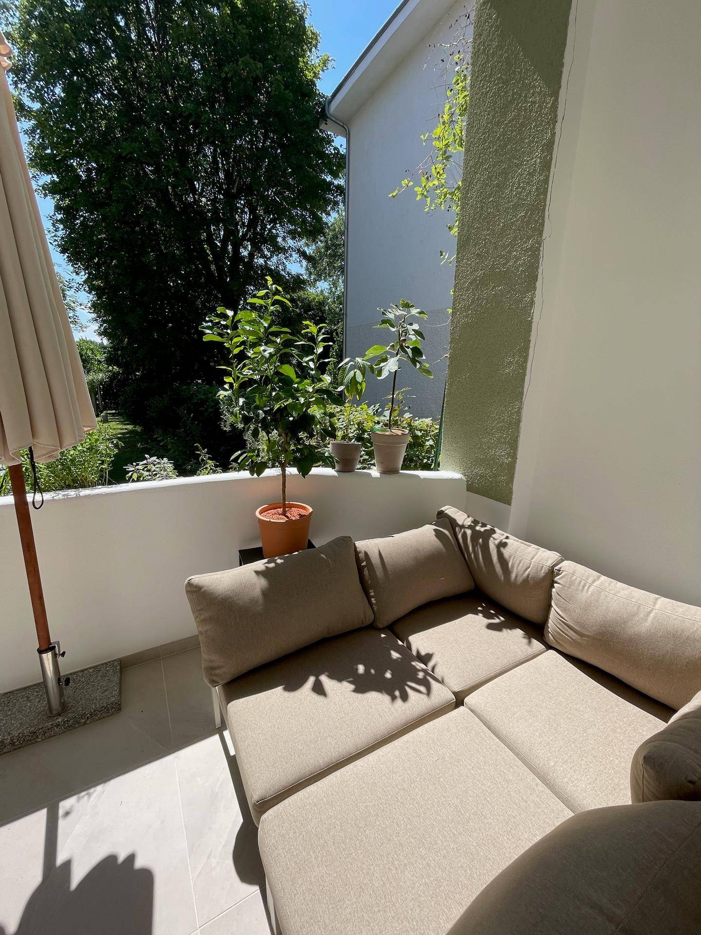 Sonniger Balkon mit beigem Loungesofa, Pflanzen und Blick ins Grüne.