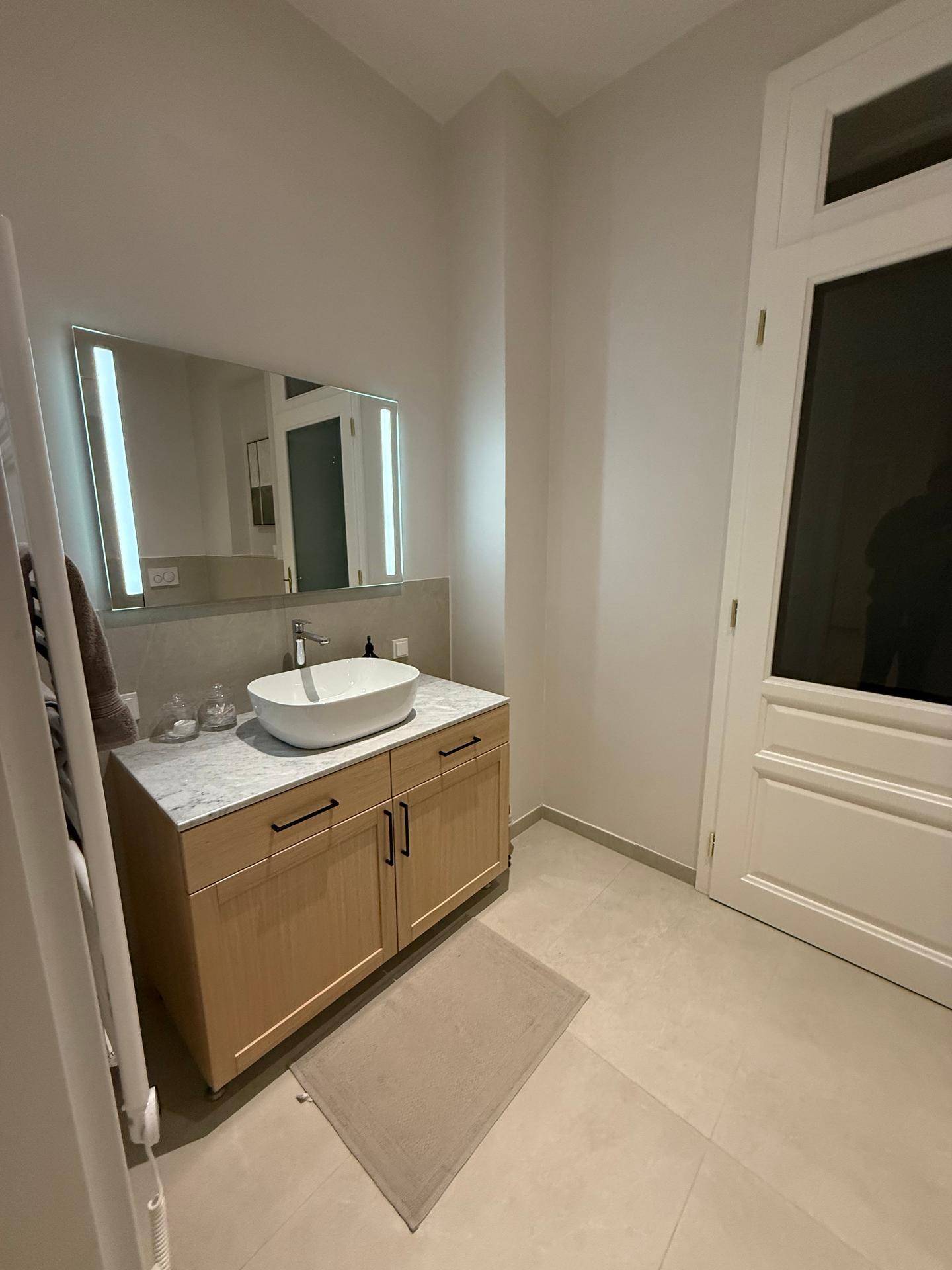 Modernes Gäste-WC mit Einzelwaschbecken, beleuchtetem Spiegel und Holzelementen.
