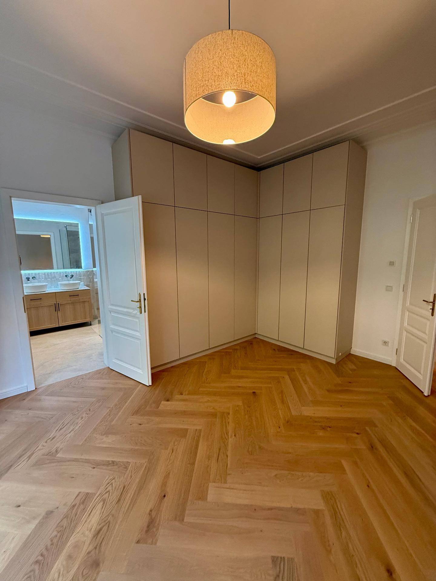 Schlafzimmer mit eleganten Einbauschränken, Fischgrätparkett und Zugang zum Badezimmer.