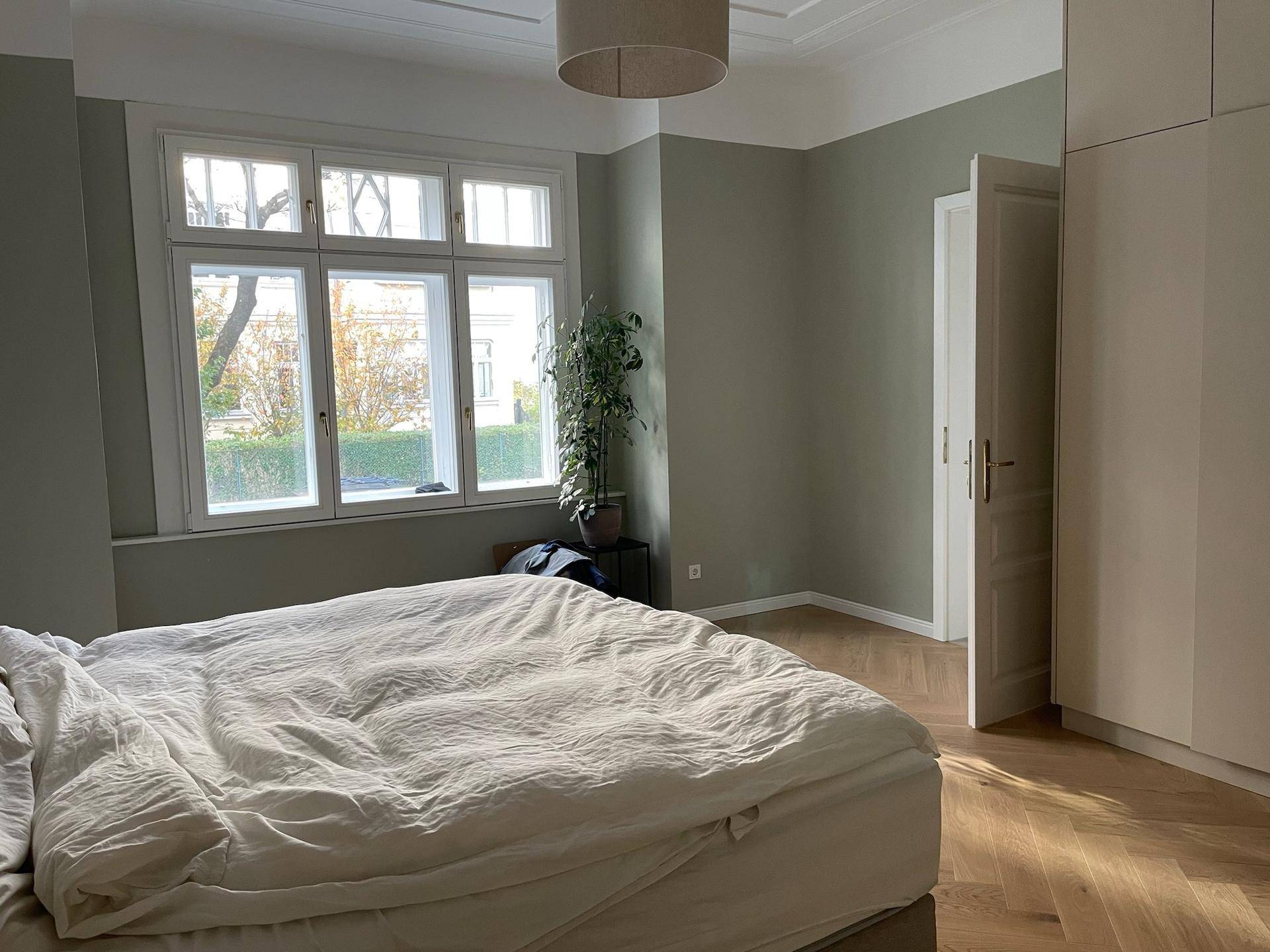 Schlafzimmer mit Doppelbett, Fischgrätparkett und großen Fenstern mit Blick ins Grüne.