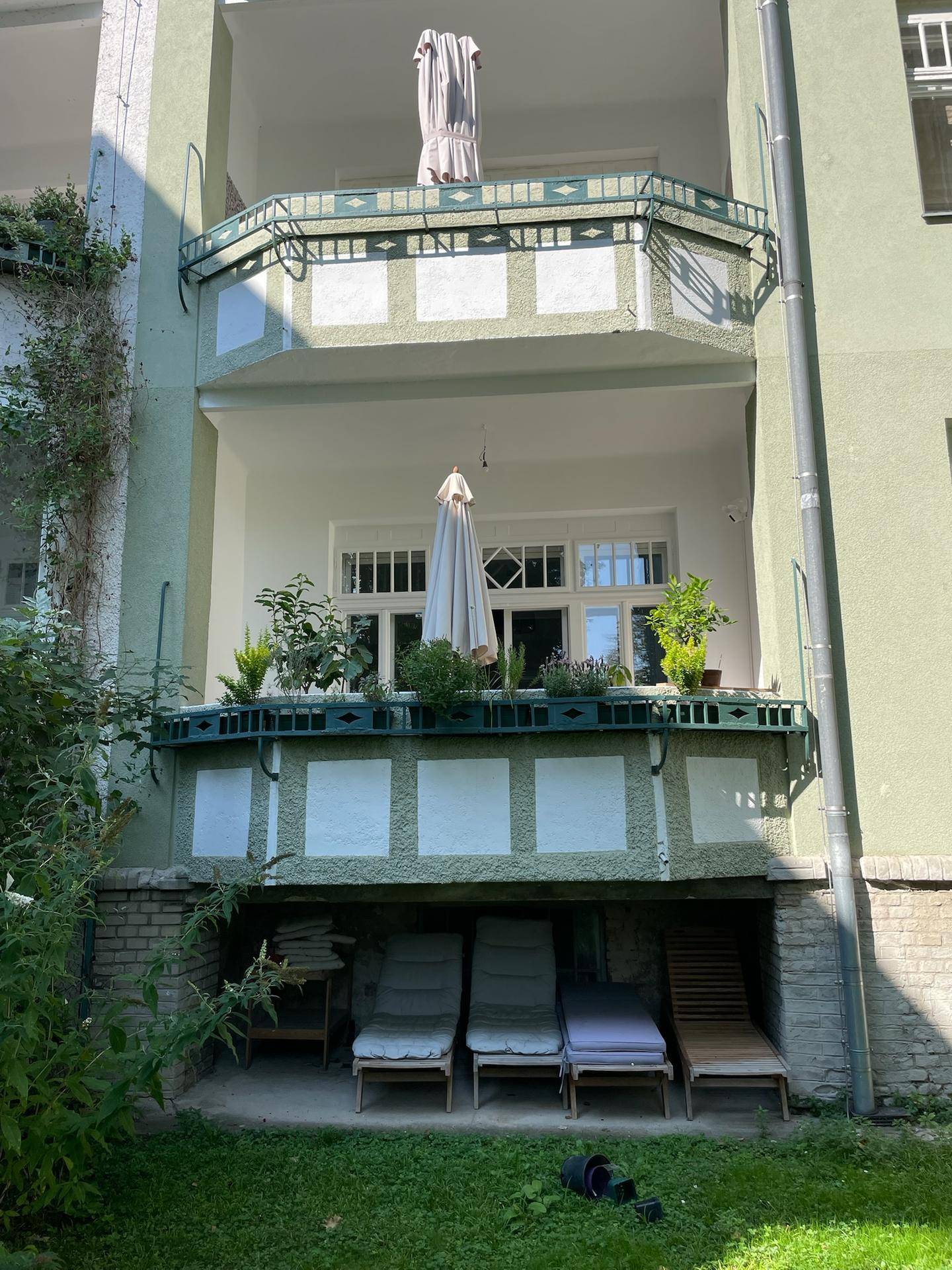 Mehrere Balkone an der Fassade eines Gebäudes mit Pflanzen und Liegestühlen im unteren Bereich.