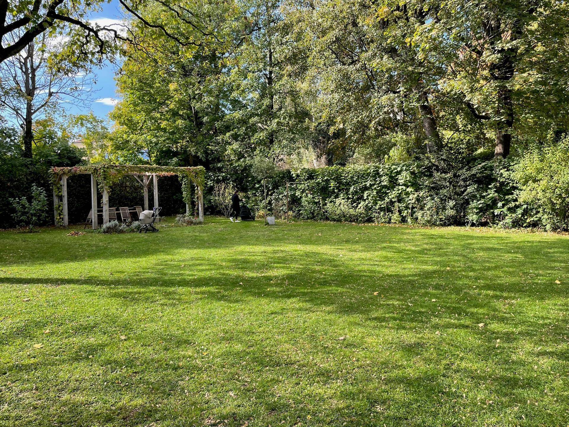 Großer, gepflegter Garten mit Rasenfläche, alten Bäumen und einer Pergola im Hintergrund.