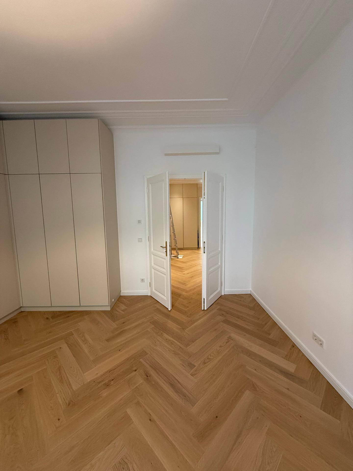 Helles Schlafzimmer mit Fischgrätparkett und praktischen Einbauschränken.