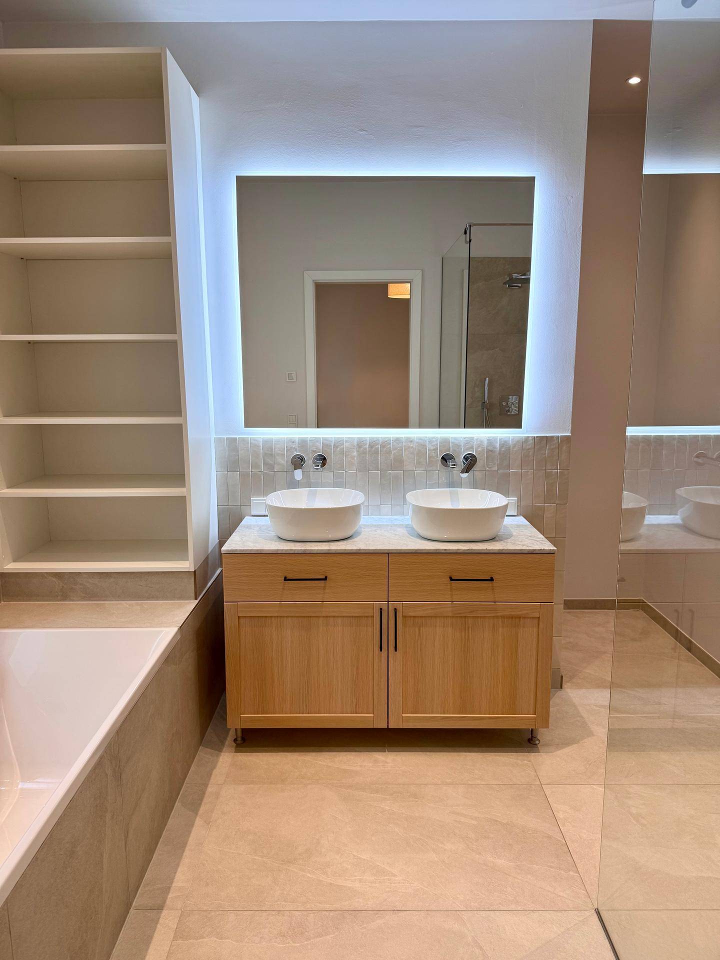 Doppelwaschbecken mit modernem Unterschrank und beleuchtetem Spiegel im Badezimmer.
