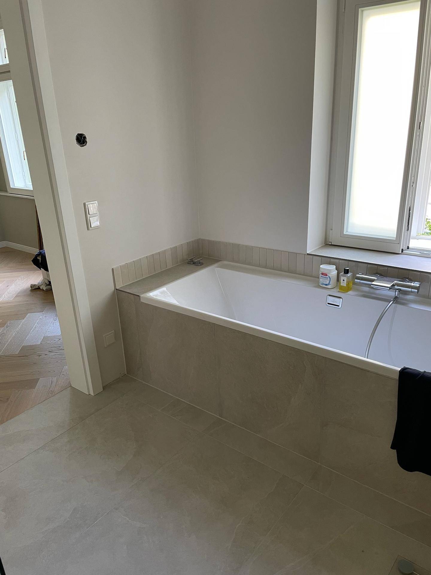 Eingebaute Badewanne mit Fliesenverkleidung und Fenster für natürliches Licht.