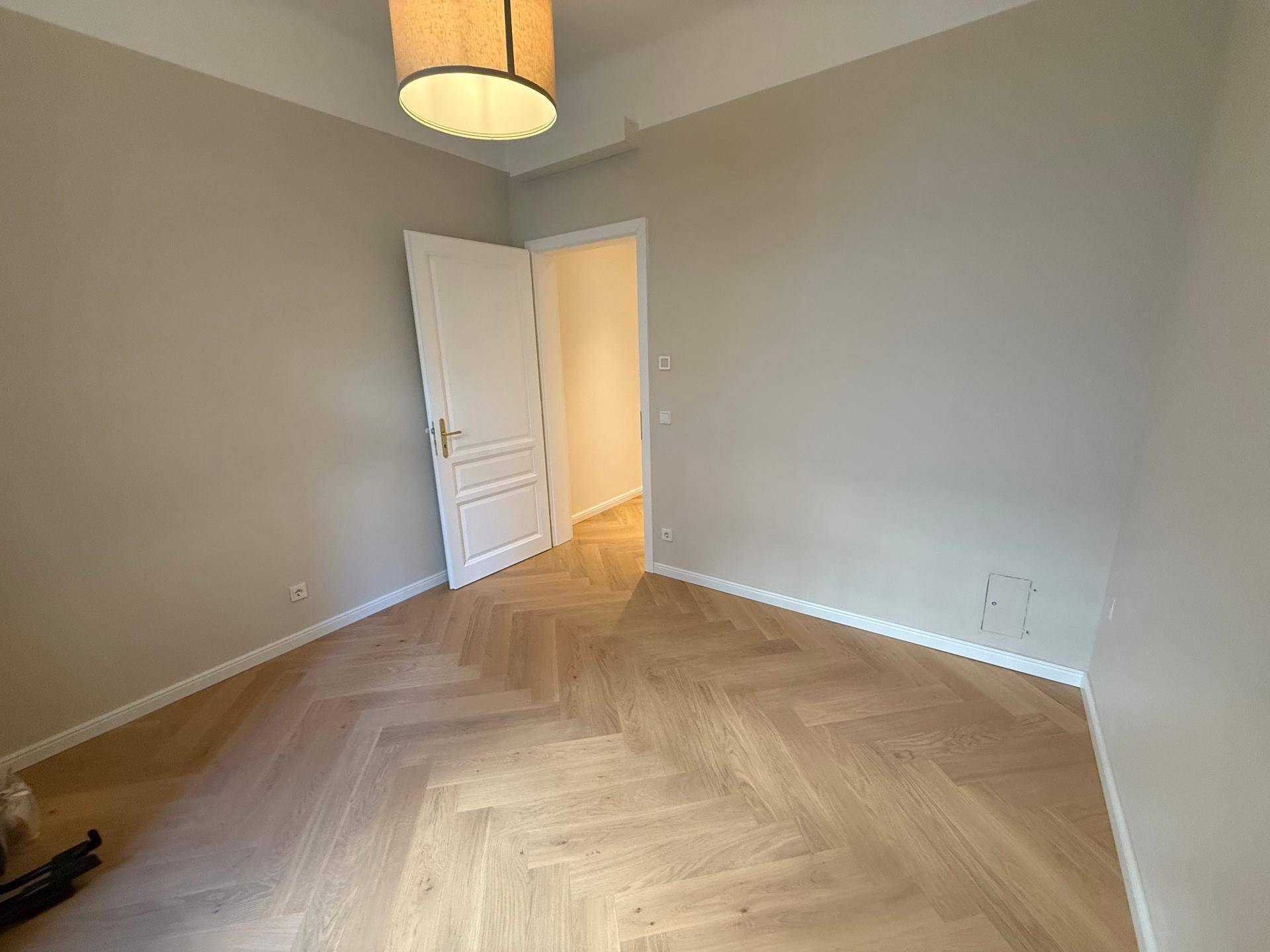 Helles Zimmer mit Fischgrätparkett und neutralen Wänden, ideal als Schlaf- oder Arbeitszimmer.