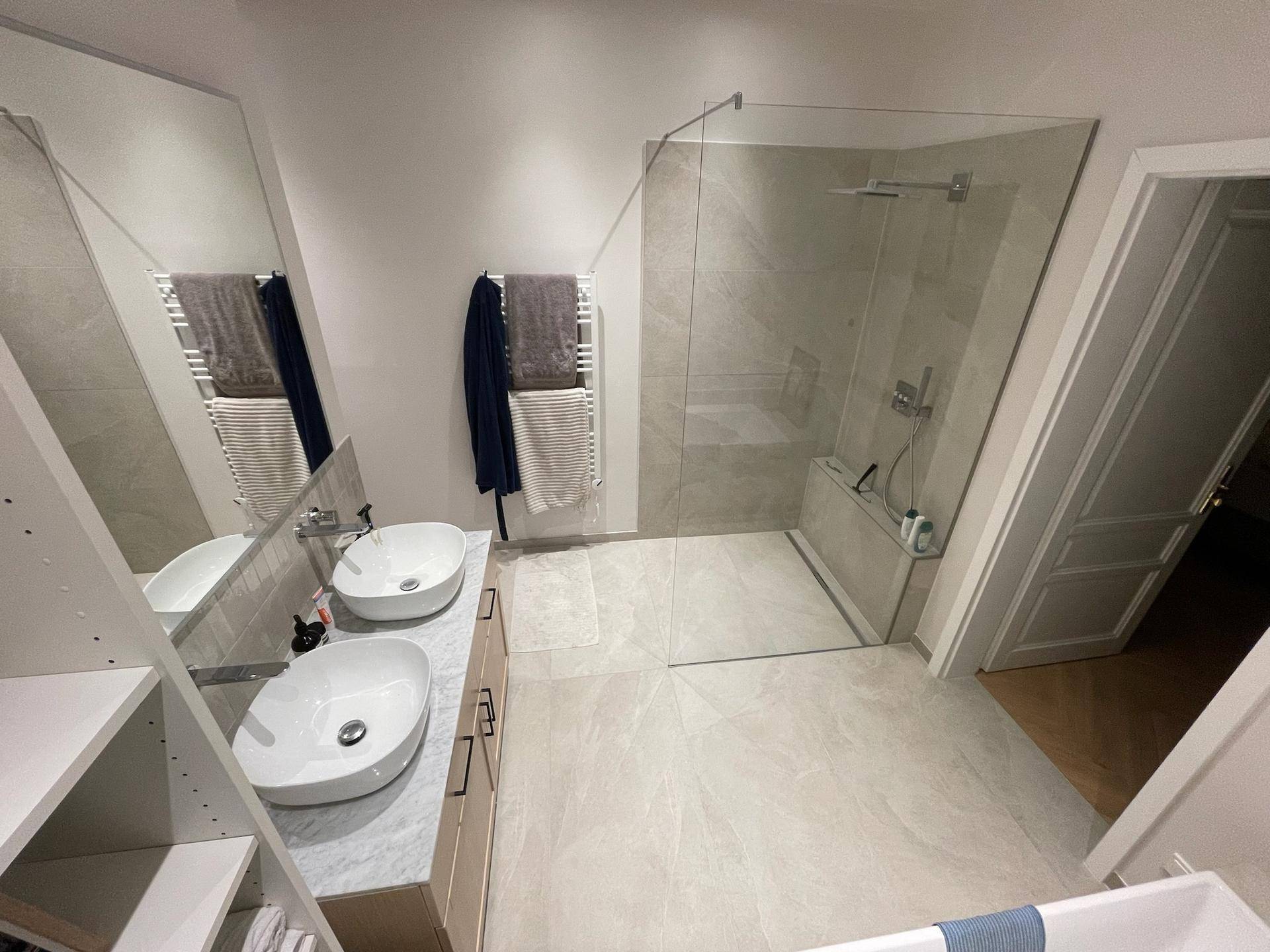 Geräumiges Badezimmer mit Doppelwaschbecken, Badewanne und großer Glasdusche.