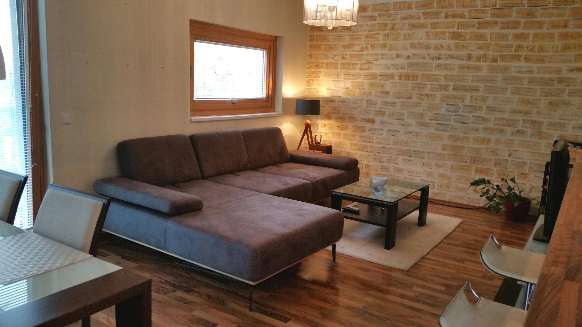 Heller Wohn- und Essbereich mit bequemer Couch, Holzboden und dekorativer Ziegelwand.