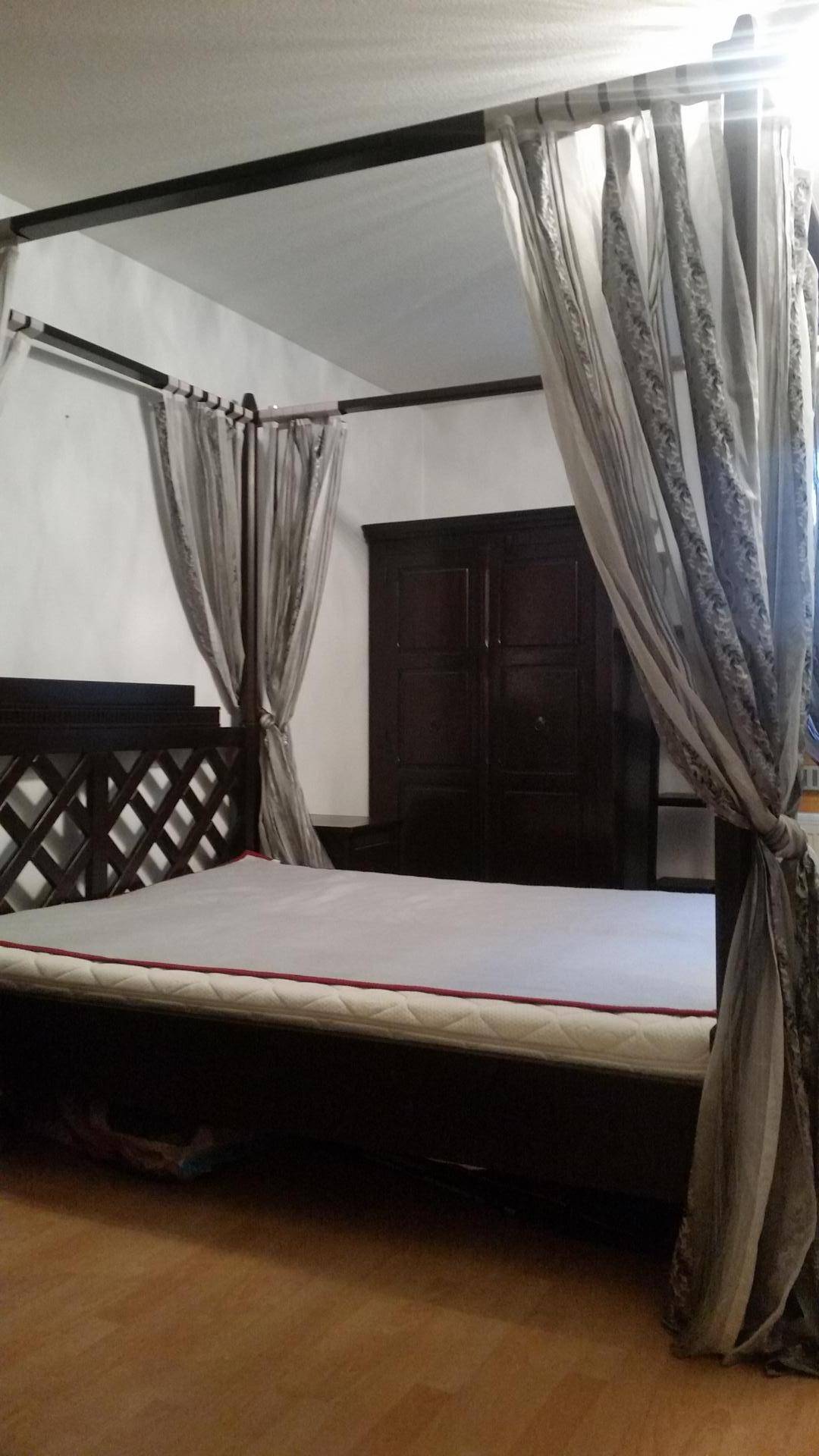 Schlafzimmer mit dunklem Himmelbett, passendem Kleiderschrank und Holzboden.